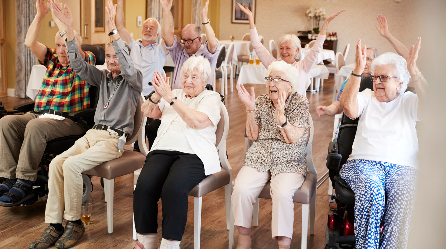 Petit groupe de seniors réunis autour d'une table travaillant ensemble sur un jeu de mémoire ou puzzle dans une salle d'activités lumineuse, lumière naturelle latérale